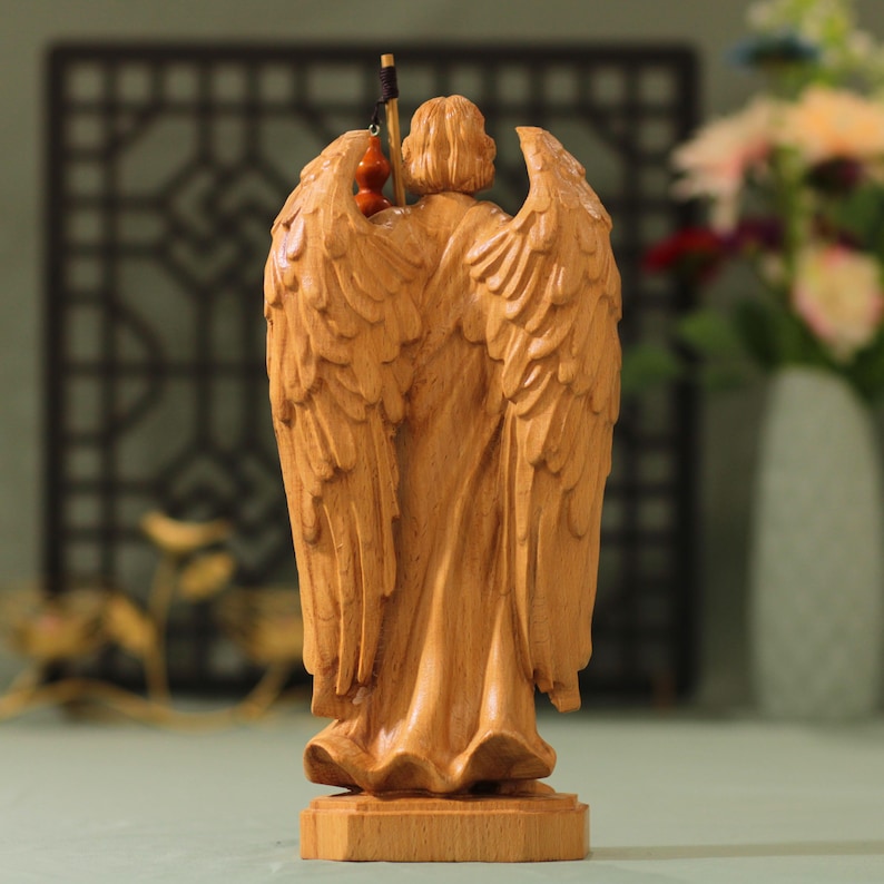 May include: A wooden sculpture of an angel with wings outstretched, carved in a light brown color. The angel is holding a small gourd in its hand.