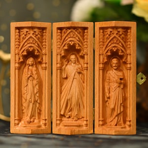 May include: A wooden triptych featuring carved religious figures. The hinged panels display detailed relief carvings of three figures within arched frames. The wood has a warm, natural tone, and the carvings showcase intricate details.