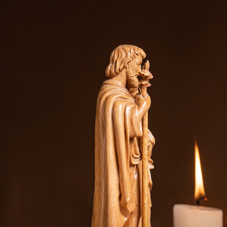 May include: A wooden figurine of a man with a beard, wearing a robe and holding a staff. The figurine is carved in detail and has a warm, natural wood tone.