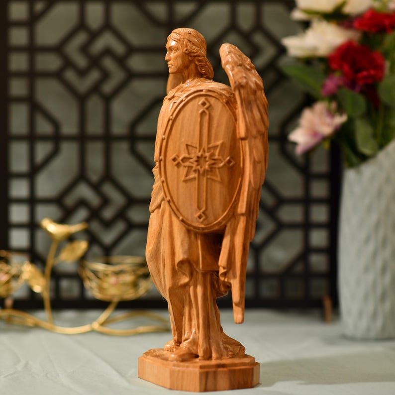May include: A wooden sculpture of an angel holding a shield with a cross and a star design. The angel is standing on a wooden base.