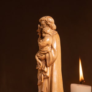 May include: A wooden sculpture of a man holding a child. The sculpture is carved in a realistic style and depicts the man holding the child close to his chest. The sculpture is painted in a natural wood tone.