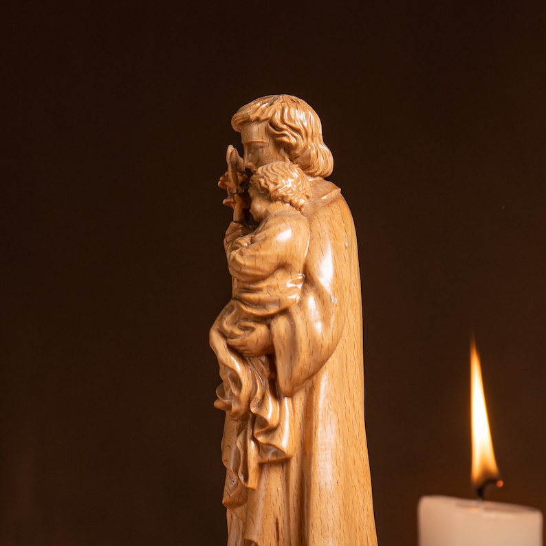 May include: A wooden sculpture of a man holding a child. The sculpture is carved in a realistic style and depicts the man holding the child close to his chest. The sculpture is painted in a natural wood tone.