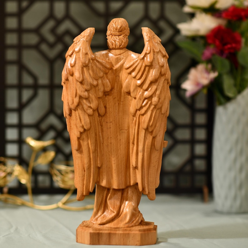 May include: A wooden sculpture of an angel with outstretched wings. The angel is carved in a light brown wood and has a detailed design.