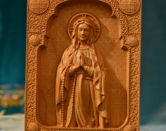 May include: A wooden carving of the Virgin Mary with a halo and rosary beads. The carving is framed in a detailed wooden frame with ornate designs.