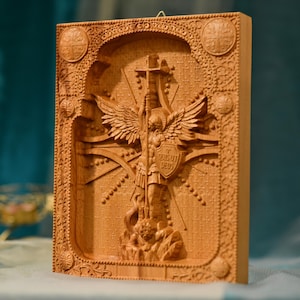 May include: A wooden carving of an angel with wings spread wide, holding a cross and standing on a serpent. The angel is wearing armor and a shield with the text "QUI UT DEUS" on it. The carving is surrounded by a decorative frame.