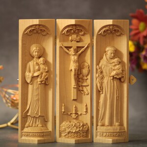Puede incluir: Un tríptico de madera con tres paneles. El panel izquierdo presenta una imagen tallada de Nuestra Señora de Fátima, el panel central presenta una imagen tallada de Jesús en la cruz y el panel derecho presenta una imagen tallada de San Antonio.