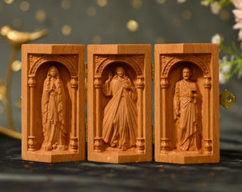 Könnte beinhalten: Ein dreiteiliges Holztriptychon mit drei geschnitzten Tafeln, die religiöse Figuren darstellen. Die linke Tafel zeigt die Jungfrau Maria, die mittlere Tafel zeigt Jesus Christus und die rechte Tafel zeigt einen Heiligen.