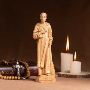 May include: A wooden statue of Saint Martin de Porres, a Catholic saint, standing with his hands clasped in prayer. The statue is on a wooden base with the inscription "St. Martino de Porres". The statue is surrounded by two lit candles and a rosary.