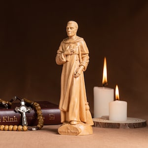 May include: A wooden statue of Saint Martin de Porres, a Catholic saint, standing with his hands clasped in prayer. The statue is on a wooden base with the inscription "St. Martin de Porres". The statue is in front of two white candles.