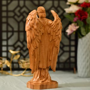 May include: A wooden angel figurine with outstretched wings. The angel is carved from a light brown wood and has a detailed design.