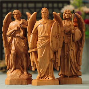 May include: Three wooden angel figurines, each with wings and a different pose. The angel in the center holds a sword and shield, while the angel on the left holds a scroll and the angel on the right holds a staff.