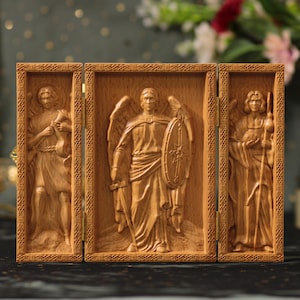 May include: A wooden triptych with carved relief panels of angels. The central panel shows an angel with a shield and sword. The side panels depict angels holding objects. The wood has a warm, natural tone.