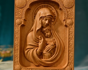 May include: A wooden carving of the Virgin Mary holding the baby Jesus. The carving is detailed and intricate, with a carved frame and a halo around the Virgin Mary's head.
