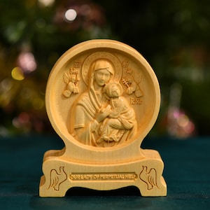 May include: A wooden carving of Our Lady of Perpetual Help, a Catholic icon depicting Mary holding the baby Jesus. The carving is on a small wooden stand with the words "Our Lady of Perpetual Help" inscribed on the front.