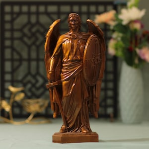 Könnte beinhalten: Eine bronzefarbene Statue eines Engels mit großen Flügeln, der ein Schwert und einen Schild hält. Der Engel ist in einem fließenden Gewand dargestellt und steht auf einem rechteckigen Sockel. Der Schild hat ein detailliertes Emblem.