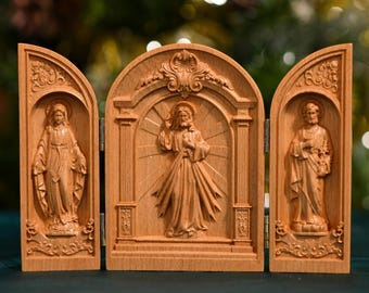 Könnte beinhalten: Ein dreiteiliges Holzrelief mit drei geschnitzten Tafeln, die religiöse Figuren darstellen. Die mittlere Tafel zeigt Jesus Christus mit offenem Herzen, die linke Tafel die Jungfrau Maria und die rechte Tafel den Heiligen Josef.