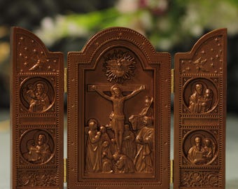 May include: A brown, hinged triptych depicting the crucifixion of Jesus Christ. The central panel shows Jesus on the cross, surrounded by figures. Side panels feature religious figures in circular frames, with stars and decorative elements.