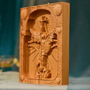 May include: A wooden carving of an angel with wings spread wide, holding a cross and a shield with the text "VIGILAT DEUS" on it. The carving is surrounded by intricate details and a decorative frame.