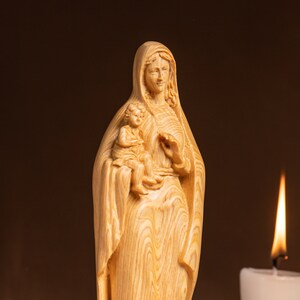 May include: A wooden statue of the Virgin Mary holding a baby Jesus. The statue is carved from light-coloured wood and has a detailed, realistic design.