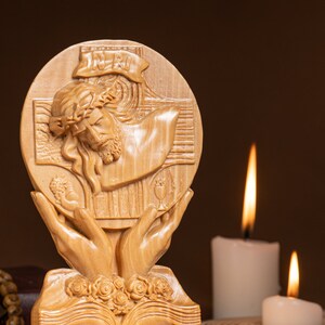 May include: A wooden carving of Jesus Christ on the cross, with the words "INRI" above his head. The carving is surrounded by two hands holding a chalice and a wheat stalk. The carving is on a wooden base with a floral design.