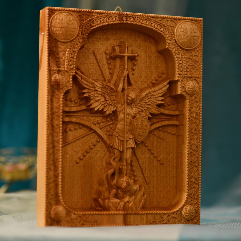 May include: A wooden carving of an angel with wings spread wide, holding a cross and a spear. The angel is standing on a dragon, and the carving is surrounded by an ornate frame.