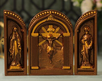 May include: A three-panel wooden triptych with gold accents. The center panel depicts a figure on a cross with a banner above that reads "INRI". The left panel shows a figure with a rosary and the right panel shows a figure holding a book.