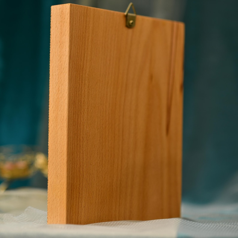 May include: A wooden frame with a light brown finish. The frame has a metal hook on the top for hanging.