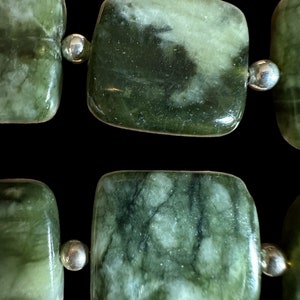 May include: A close-up of a green and white stone bead necklace. The beads are square shaped and have a marbled pattern. The necklace is made with silver spacers.