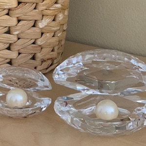 May include: Two crystal clam shell boxes with a pearl inside each. The larger clam shell is open and the smaller clam shell is closed.