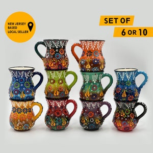 May include: A set of colorful ceramic mugs with intricate floral patterns. Each mug features a unique color scheme, including blue, green, orange, and red, with a curved handle. The mugs are stacked and displayed against a white background. Text reads: "SET OF 6 OR 10" and "NEW JERSEY BASED LOCAL SELLER".