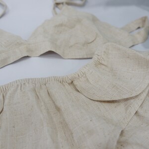 May include: A beige linen bralette and matching shorts with a ruffled trim. The bralette has adjustable straps.