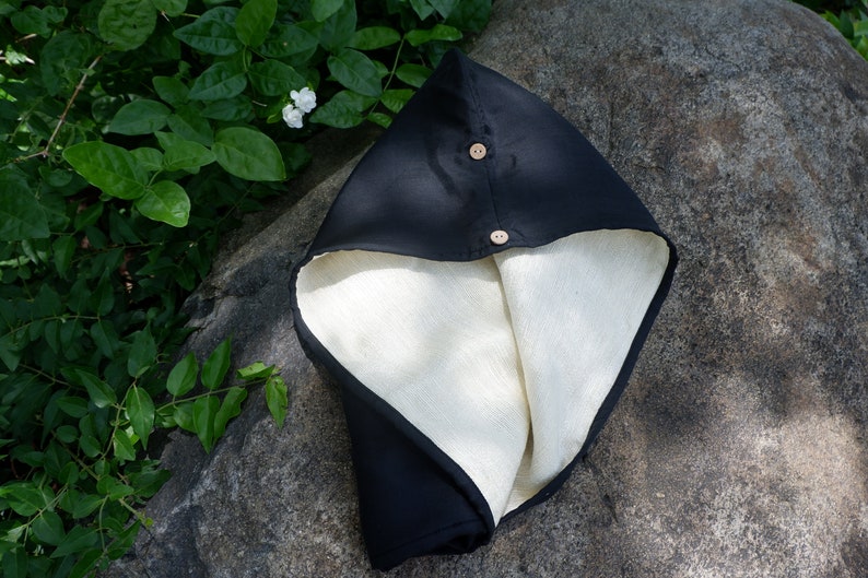 May include: A black hooded scarf with a white lining and two wooden buttons. The scarf is folded and lying on a gray rock.