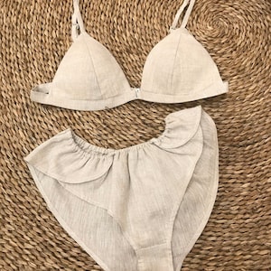 May include: A beige linen lingerie set with a triangle bra and high-waisted panties with a ruffled trim.