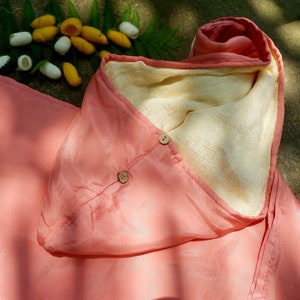 Pode incluir: Um envoltório para bebê com capuz rosa e creme com dois botões de madeira. O envoltório é feito de um tecido macio e sedoso.