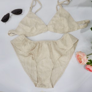 May include: A beige linen lingerie set with a triangle bra and ruffled panty.