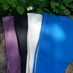May include: Four fabric headbands in different colors: purple, black, white, and blue. The headbands are laid out on a gray rock.