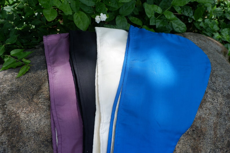 May include: Four fabric headbands in different colors: purple, black, white, and blue. The headbands are laid out on a gray rock.