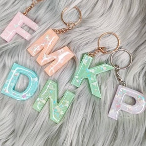 May include: Five pastel-coloured resin letter keyrings with gold key rings. The letters spell out "F.M.K.D.P."