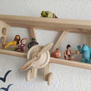 May include: A wooden airplane shelf with various cartoon character figurines, including a lion, a girl in a red hood, a green monster, a fish, a man in a turban, and a blue monster.