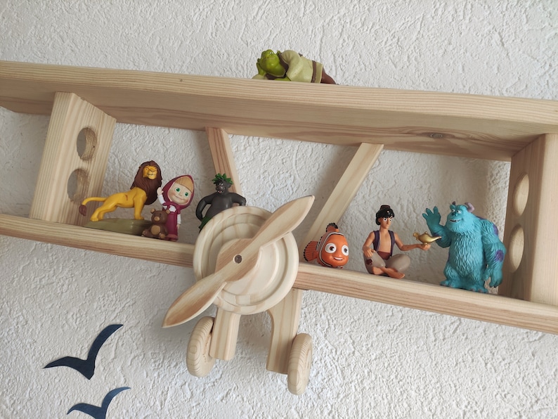 May include: A wooden airplane shelf with various cartoon character figurines, including a lion, a girl in a red hood, a green monster, a fish, a man in a turban, and a blue monster.
