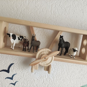 May include: Wooden airplane shelf with a cow, donkey, goat, horse, and sheep figurines. The shelf is painted in a natural wood color.