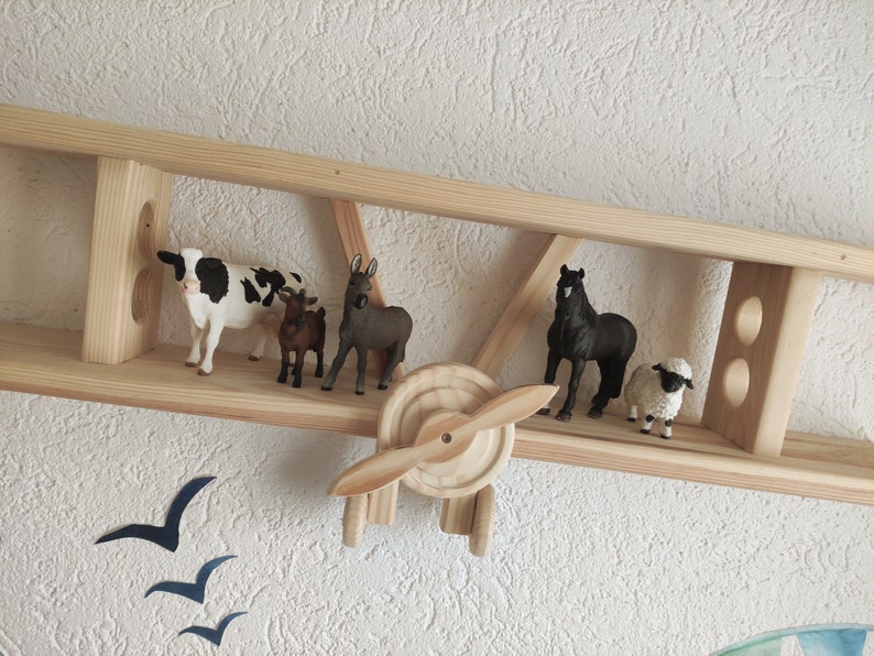 May include: Wooden airplane shelf with a cow, donkey, goat, horse, and sheep figurines. The shelf is painted in a natural wood color.