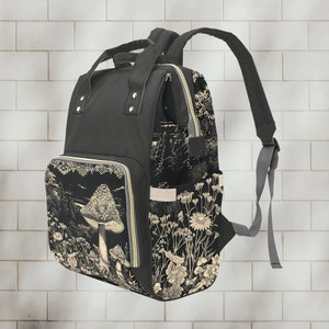 May include: A black canvas backpack with a floral and mushroom print. The backpack has a zippered front pocket and adjustable straps.