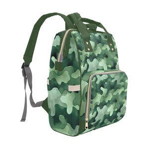 May include: Green camouflage backpack with multiple compartments and gold zippers. The backpack has adjustable shoulder straps and a top handle. The camouflage pattern features shades of green and white. The backpack is designed for carrying items.