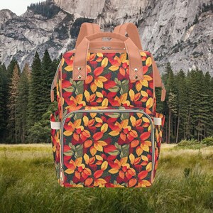May include: A brown and tan backpack with a fall leaf pattern. The backpack has a large main compartment and two smaller pockets on the sides. The backpack is made of a durable fabric and has a zipper closure.