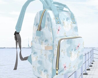 May include: A light blue diaper bag with a dragonfly print and gold accents. The bag has multiple pockets and a zipper closure.