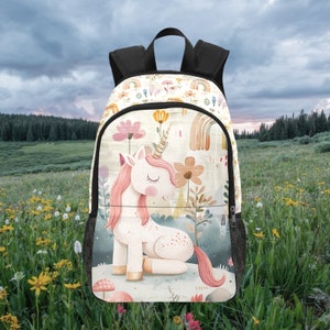 May include: A white and pink unicorn backpack with a floral and rainbow design. The backpack has a black zipper and adjustable straps.
