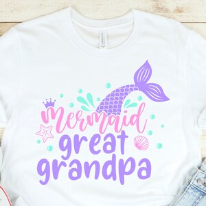 May include: White t-shirt with a purple mermaid tail, pink crown, and the text "Mermaid Great Grandpa" in purple and pink.