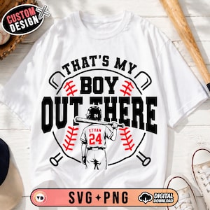 May include: White t-shirt with a baseball-themed graphic. The design features the text "THAT'S MY BOY OUT THERE" in black, with a baseball player illustration and the name "Ethan" and the number "24". The design includes baseball bats and stitching.