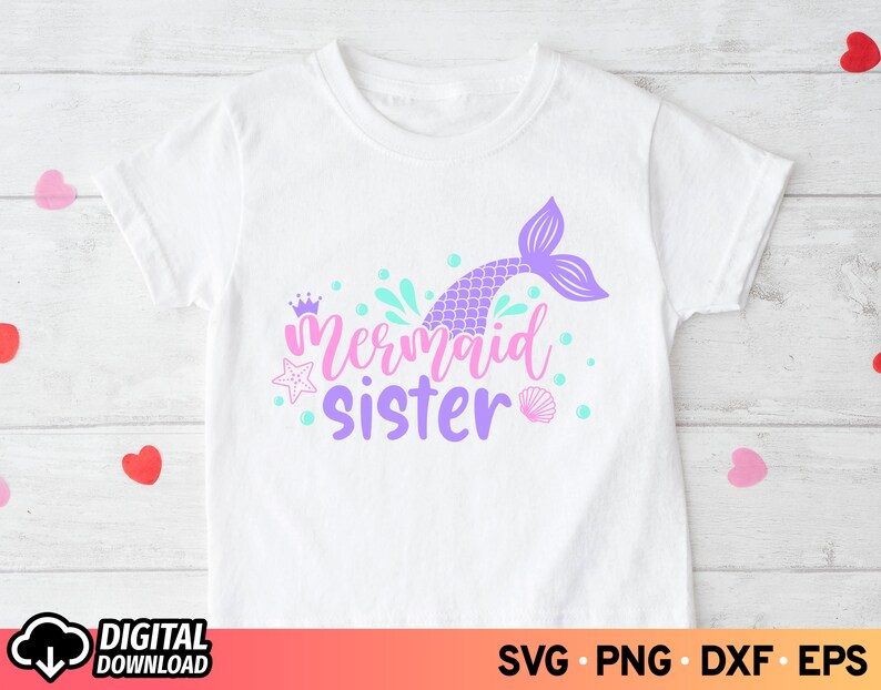 May include: A white t-shirt with a purple mermaid tail, a crown, and the text "Mermaid Sister" in purple.